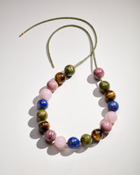 Alphabet city downtown necklace including Unakite, Tiger's eye, Rhodonite, Rose quart  and Lapis lazuli semi precious spheres on white background