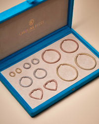 Blue velvet earrings case holding 18k florentine frosted finish gold Round Huggies, Oval Huggies, Small Round Hoops, Small Cuore Hoops, Large Round Hoops and Extra Large Oval Hoops earrings